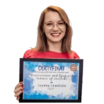 Uśmiechnięta kobieta w okularach i czerwonej bluzce z certyfikatem trenera pracy z emocjami Neuroscience & Epigenetics Trainer of Emotions